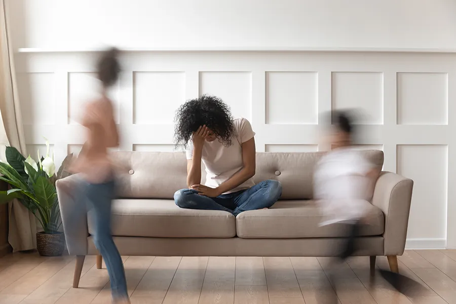ADHD-Treatment-Clinic A parent sits exhausted on a couch while kids run around her. Schedule treatment for ADHD and ADD from Markham Natural Health Centre in Greater Toronto.