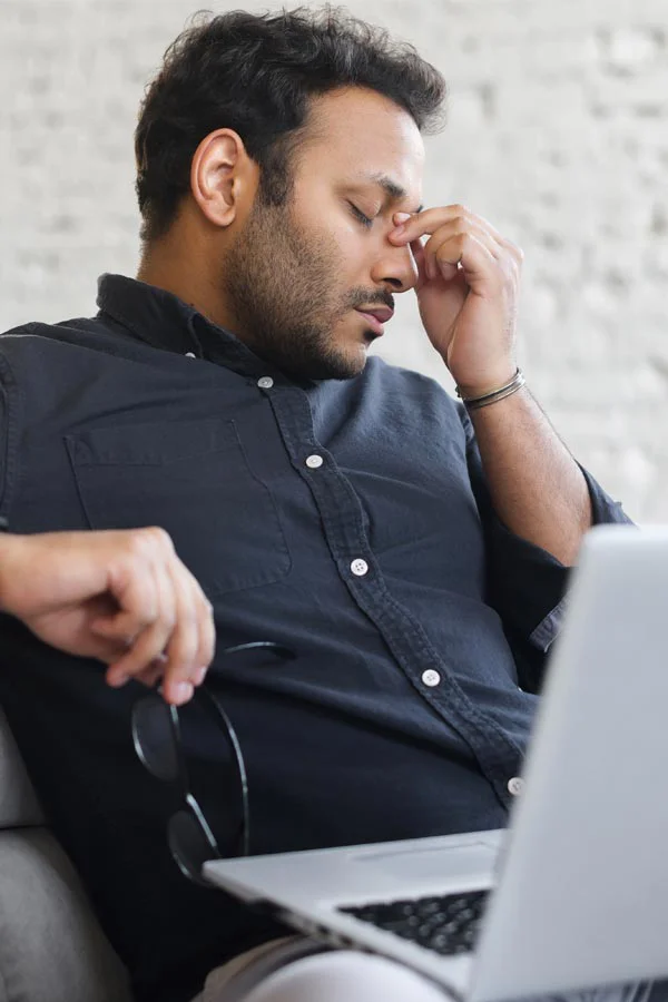 Adrenal-Fatigue-Treatment A middle-aged man with a laptop closing his eyes and rubbing his nose. He needs treatment for Adrenal Fatigue Syndrome from Markham Natural Health Centre in Greater Toronto.