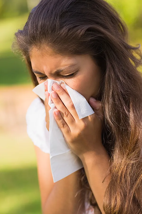 Allergy-Treatment-Treatment A woman with long brown hair sneezes into a handkerchief outdoors. Get allergy treatment services from Markham Natural Health Centre in Greater Toronto.