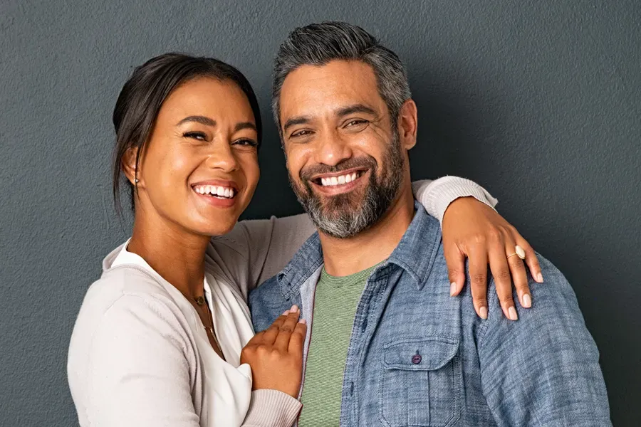 Bioidentical-Hormone-Therapy-Doctor A middle-aged couple with their arms around each other standing against a gray background and smiling, happy with the bioidentical hormone therapy they received from Markham Natural Health Centre in Greater Toronto.
