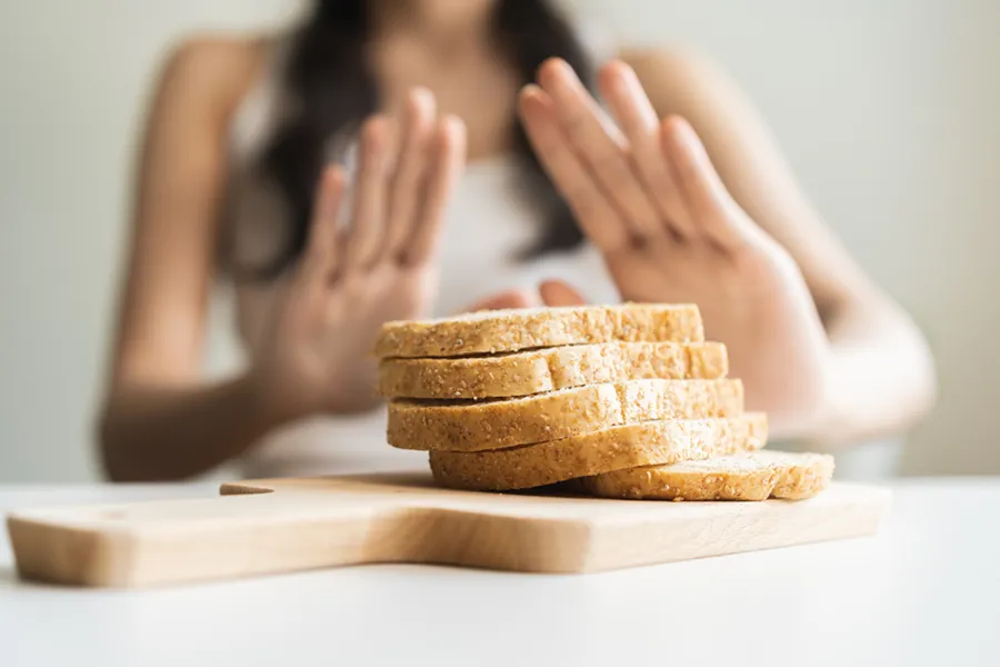 Celiac-Disease-Clinic Close up of a stack of bread slices on a cutting board with a woman's hands behind them, refusing to eat. Get treatment for Celiac Disease from Markham Natural Health Centre in Greater Toronto.