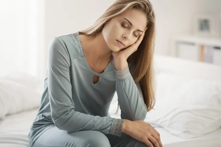 Depression-Clinic A woman sits on the edge of her bed with her head in her hands. Schedule treatment for depression from Markham Natural Health Centre in Greater Toronto.