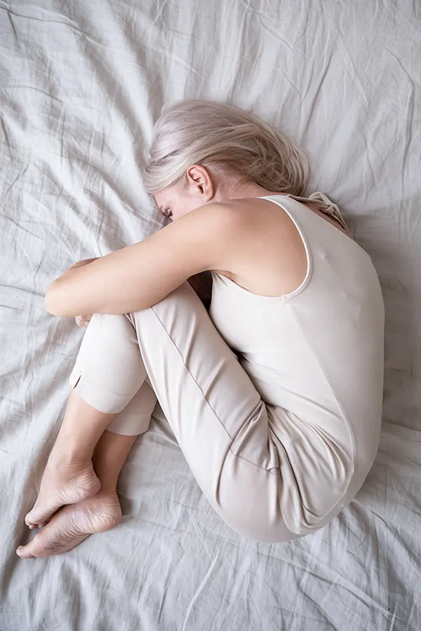 Depression-Treatment A woman curls up in the fetal position on her bed. Get treatment for depression from Markham Natural Health Centre in Greater Toronto.