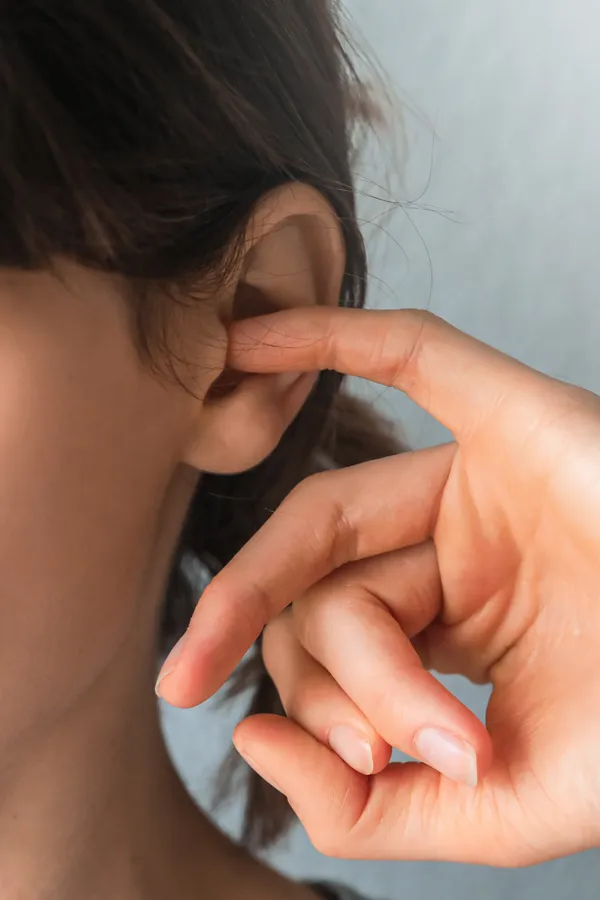 Ear-Candling-Treatment A woman with her finger in her ear. Get ear candling services from Markham Natural Health Centre in Greater Toronto.