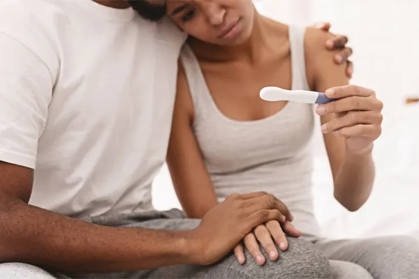 Infertility-Clinic A black couple sits on a bed, disappointed with the negative results of a pregnancy test. Get treatment for infertility from Markham Natural Health Centre in Greater Toronto.