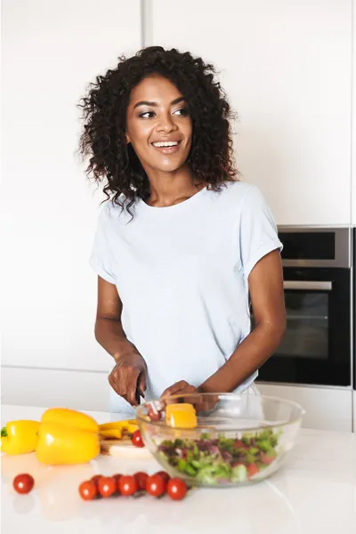 Irritable-Bowel-Syndrome-Treatment Image featuring a smiling woman chopping vegetables for a salad in a bright, white kitchen. Markham Natural Health Centre offers Irritable Bowel Syndrome Treatment and Digestive Support in Greater Toronto.