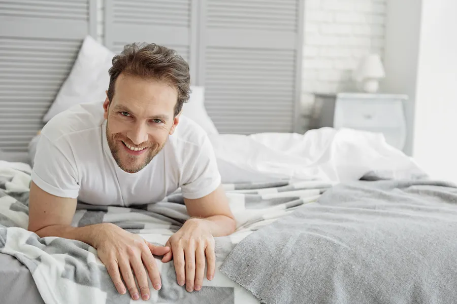 Low-Libido-in-Men-Doctor A dirty-blonde haired man lays on his stomach in bed smiling. Schedule treatment for low libido in men from Markham Natural Health Centre in Greater Toronto.