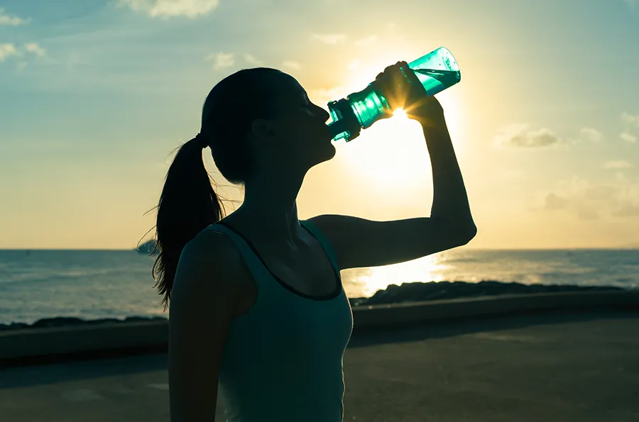 Natural-Detoxification-Clinic A woman hydrates during a beach run at sunset. Schedule natural detoxification treatment from Markham Natural Health Centre in Greater Toronto.