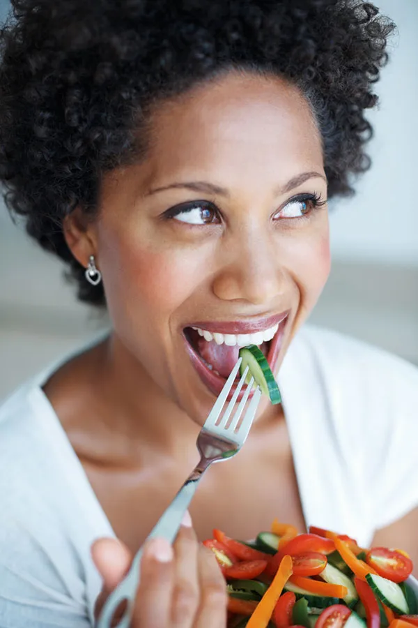 Natural-Detoxification-Treatment A Black woman smiles while eating a healthy salad. Get natural detoxification treatment from Markham Natural Health Centre in Greater Toronto.