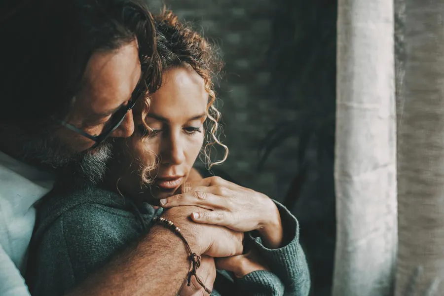 Neurodegenerative-Disorders-Therapy A man embraces a woman from behind in a dimly lit room, their somber expressions showing concerns about a neurodegenerative disease they will get treated by Markham Natural Health Centre in Greater Toronto.