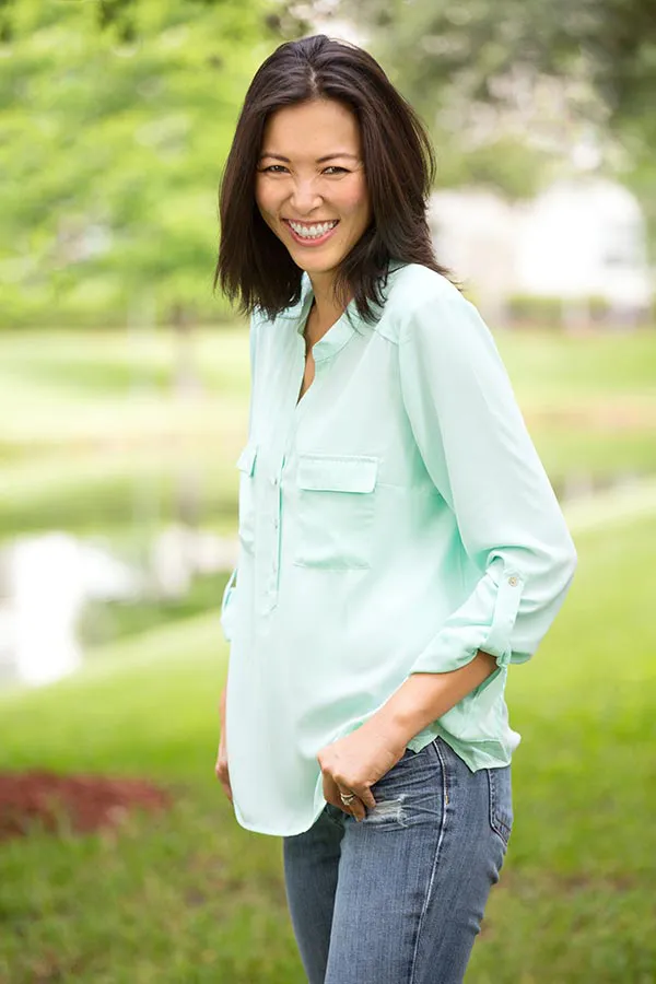 Perimenopause-Treatment A middle-aged brunette woman in a light green button-up shirt stands outside smiling, happy with her perimenopause treatment from Markham Natural Health Centre in Greater Toronto.