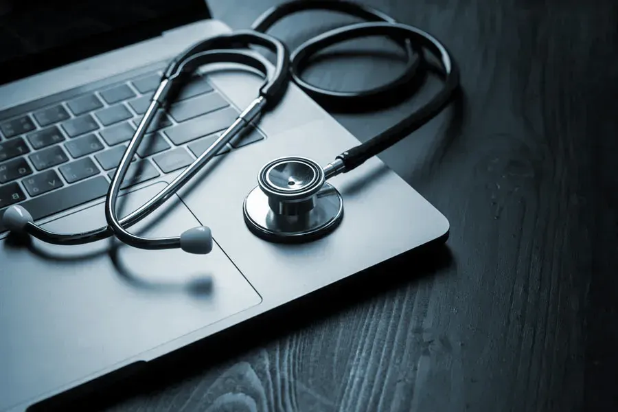 Telemedicine-Doctor An open laptop with a stethoscope lying on it on a wooden table, symbolizing telemedicine care from Markham Natural Health Centre in Greater Toronto.