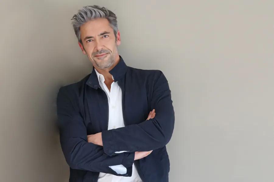 Testosterone-Low-T-Solutionsn-Clinic A middle-aged man in a white shirt and dark blue jacket leans against a gray wall smiling. Get testosterone for Low T from Markham Natural Health Centre in Greater Toronto.