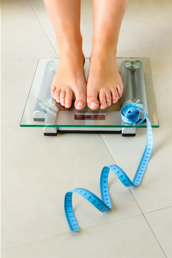 Weight-Loss-Resistance-Treatment Close-up of a woman's feet standing on a scale, with measuring tape by her toes, getting treatment for weight loss resistance from Markham Natural Health Centre in Greater Toronto.